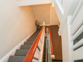 A carpeted staircase with a wooden handrail and a small table with a plant and decoration at the bottom at Russell House in Paignton