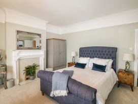 A bedroom with a blue upholstered bed a white fireplace a gray wardrobe and two wooden bedside tables with lamps at Russell House in Paignton