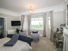 A bedroom with a bed a blue throw two white chairs with blue cushions a wall-mounted TV and a dressing table with a kettle at Russell House in Paignton