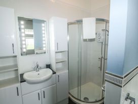 A bathroom with a sink and cabinet unit next to a corner shower enclosure with a towel hanging inside Russell House in Paignton