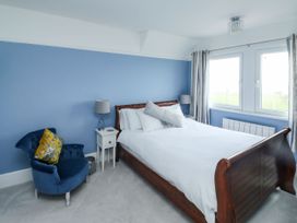 A bedroom with a wooden bed white bedding blue walls a blue chair with a yellow cushion and two bedside tables with lamps at Russell House in Paignton