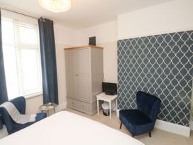 A bedroom with two blue chairs a gray wardrobe a small white table with a TV and a window with blue curtains at Russell House in Paignton