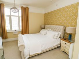 A bedroom with a beige upholstered bed white bedding yellow patterned wallpaper and brown curtains at Russell House in Paignton