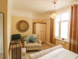 A bedroom with a bed, armchair with pillows, wardrobe, window with curtains, and a small TV on a cabinet at Russell House in Paignton