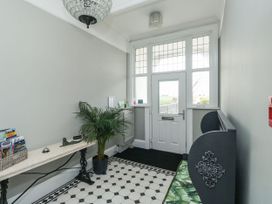 An entryway with a white door and windows a bench with a green patterned cushion a potted plant and a marble top table with brochures and decorative items at Russell House in Paignton