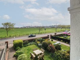 A garden with wooden picnic tables and benches behind a low brick wall next to a road with a green field and sparsely placed trees beyond Russell House in Paignton