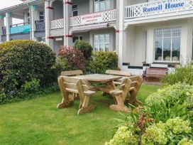 A wooden picnic table with benches on a grassy area in front of buildings with signs reading Russell House and Sefton Lodge at Russell House in Paignton