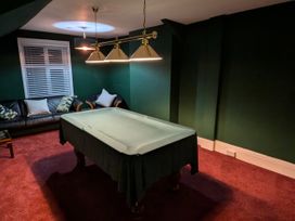A room with a covered pool table a black sofa and armchair with pillows green walls and red carpet at Russell House in Paignton