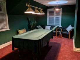 A room with a covered pool table a ceiling light black leather chairs with pillows and green walls at Russell House in Paignton