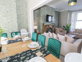 A dining table with green chairs and tableware next to a living room with sofas and a fireplace at 6 Canning Road in Colwyn Bay