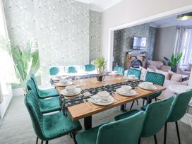 A dining room with a wooden table set with dishes and green chairs near a living room at 6 Canning Road in Colwyn Bay