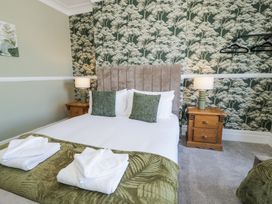 A bedroom with a bed with green pillows and throw a wooden bedside table with a lamp and folded towels on the bed at 6 Canning Road in Colwyn Bay