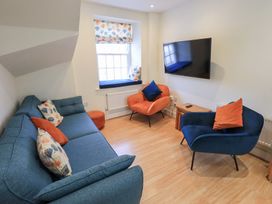 A living room with blue and orange chairs a blue sofa with patterned cushions a wall mounted tv and a window with a cushion seat at 4 Martindales Yard in Kendal