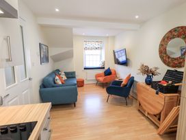 A living room with blue and orange chairs a wall mounted television and a wooden foldable dining table at 4 Martindales Yard in Kendal