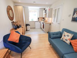 A living area with a blue armchair and a blue sofa with cushions next to an open kitchen at 4 Martindales Yard in Kendal