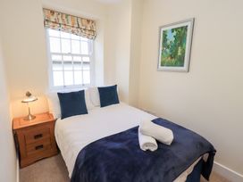 A bedroom with a double bed blue pillows and blanket bedside table with lamp window and framed artwork on wall at 4 Martindales Yard in Kendal