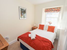 A bedroom with a bed with orange pillows and blanket by a window with floral blind at 4 Martindales Yard in Kendal