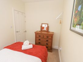 A bedroom with a wooden dresser with mirror a bed with white and orange bedding and a wall painting at 4 Martindales Yard in Kendal