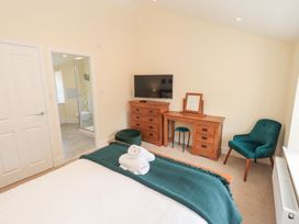 A bedroom with a bed folded towels wooden dresser TV wooden dressing table green chair and doorway to bathroom at 4 Martindales Yard in Kendal