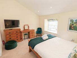 A bedroom with a bed a green chair a dresser a vanity table a pouf and a wall mounted television at 4 Martindales Yard in Kendal