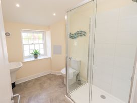 A bathroom with a shower enclosure a toilet a sink and a window with a plant on the sill at 4 Martindales Yard in Kendal