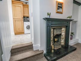 A room with a black fireplace and potted plants next to a kitchen with wooden cabinets and a washing machine at Bwthyn Llwyncaron in Rhydtalog near Llandegla
