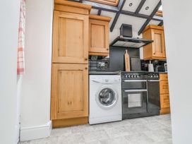 A kitchen with wooden cabinets a washing machine a black oven and a range hood at Bwthyn Llwyncaron in Rhydtalog near Llandegla