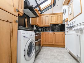 A kitchen with wooden cabinets a washing machine an oven and mugs hanging on a rail at Bwthyn Llwyncaron in Rhydtalog near Llandegla