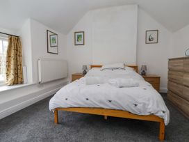 A bedroom with a bed with white bedding and towels on it two bedside tables with lamps a window with patterned curtains and a wooden chest of drawers at Bwthyn Llwyncaron in Rhydtalog near Llandegla