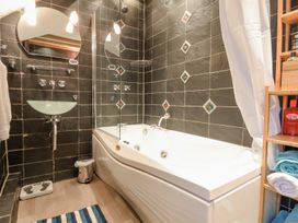 A bathroom with a bathtub glass sink mirror wooden shelving and a striped rug at Bwthyn Llwyncaron in Rhydtalog near Llandegla
