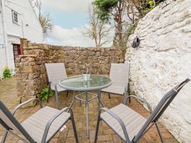 An outdoor patio area with a glass round table and four chairs surrounded by stone and white walls at Bwthyn Llwyncaron in Rhydtalog near Llandegla