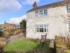An exterior view of a white house with windows a grassy garden area with two wooden chairs a stone wall and a paved driveway at Bwthyn Llwyncaron in Rhydtalog near Llandegla