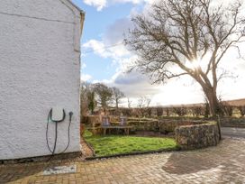 An outdoor area with a grass patch and two wooden chairs next to a stone wall and a white house wall with an electric charger at Bwthyn Llwyncaron in Rhydtalog near Llandegla