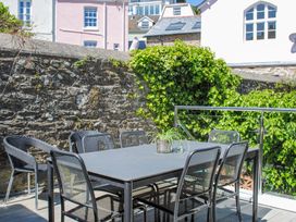 An outdoor patio area with a black table and six black chairs next to a stone wall with green ivy at 2 Russell Court Salcombe
