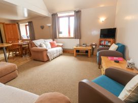 A living room with sofas and armchairs a wooden dining table and chairs a television on a stand at Henblas Cottage in Rhyd-Y-Foel