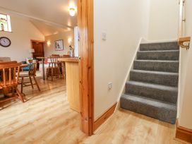A staircase with gray carpet leading to an upper floor and a wooden dining area with chairs and tables at Henblas Cottage in Rhyd-Y-Foel