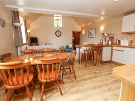 An open dining and living area with a wooden dining table and chairs a kitchen counter with stools a couch a TV and wall decorations at Henblas Cottage in Rhyd-Y-Foel