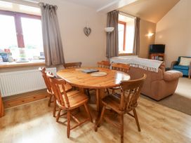 A dining area with a wooden table and six chairs next to windows with curtains and a living room with a sofa and armchair at Henblas Cottage Rhyd-Y-Foel