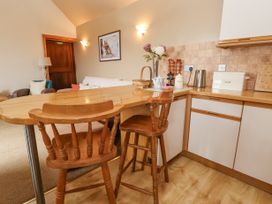 A kitchen area with wooden bar stools a countertop a bread box kettle and a living area in the background at Henblas Cottage Rhyd-Y-Foel