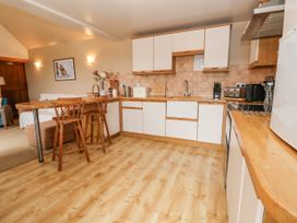 A kitchen with white cabinets and wooden countertops with two wooden chairs at a breakfast bar at Henblas Cottage in Rhyd-Y-Foel