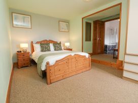 A bedroom with a wooden bed and bedside tables with lamps next to an en suite bathroom at Henblas Cottage in Rhyd-Y-Foel