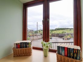 A window with two baskets of books and a flower vase on a wooden surface at Henblas Cottage in Rhyd-Y-Foel