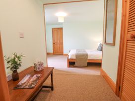 A bedroom with a wooden bed and a bedside lamp visible from a hallway with a wooden table holding flowers a tissue box and magazines at Henblas Cottage in Rhyd-Y-Foel