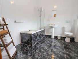 A bathroom with a bathtub shower sink toilet wooden towel rack and black marble tiles at Henblas Cottage Rhyd-Y-Foel