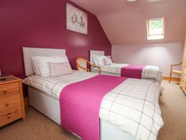 A bedroom with two single beds with pink runners and checked bedspreads a wooden dresser two wooden chairs and a skylight window at Henblas Cottage in Rhyd-Y-Foel