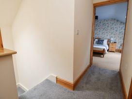 A hallway with grey carpet leading to a bedroom with a bed and wooden furniture at Henblas Cottage in Rhyd-Y-Foel