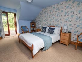 A bedroom with a double bed two wooden bedside tables two wooden chairs a small bookcase and open door to the outside at Henblas Cottage in Rhyd-Y-Foel