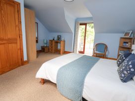 A bedroom with a bed a blue throw a wooden desk a chair and a glass door leading outside at Henblas Cottage in Rhyd-Y-Foel
