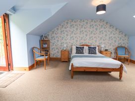 A bedroom with a wooden bed two chairs two bedside tables a bookshelf and floral wallpaper at Henblas Cottage in Rhyd-Y-Foel