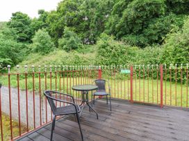 An outdoor deck with two black chairs and a round glass table surrounded by a red metal railing and green trees at Henblas Cottage in Rhyd-Y-Foel